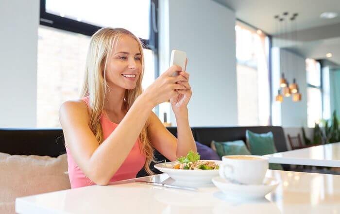 Woman smiling as she logs her salad lunch on her smartphone