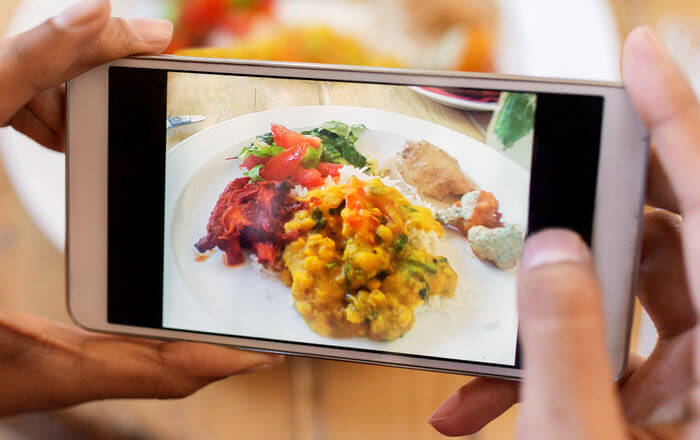 Hands holding a smartphone to photograph a plate of food for meal tracking
