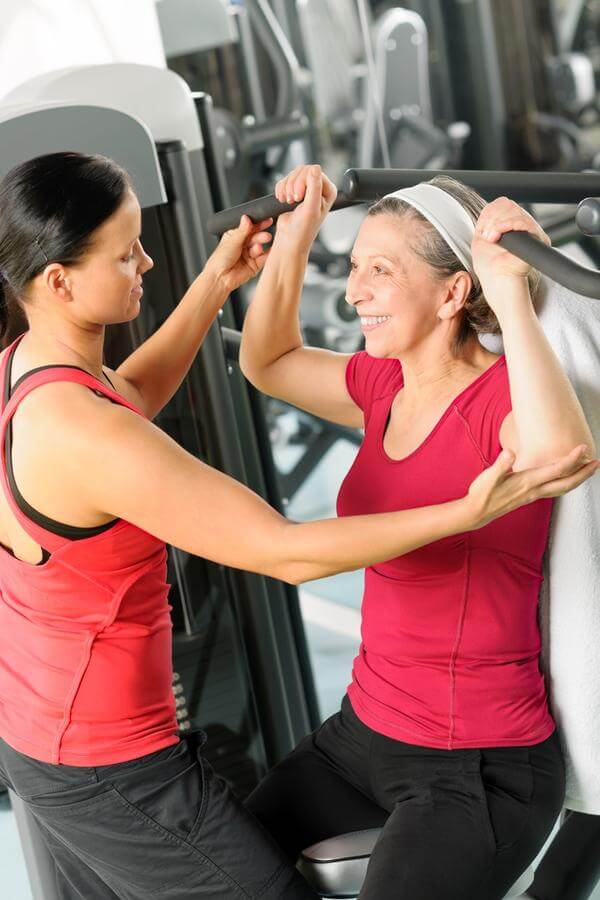 Personal trainer helping senior woman with gym equipment